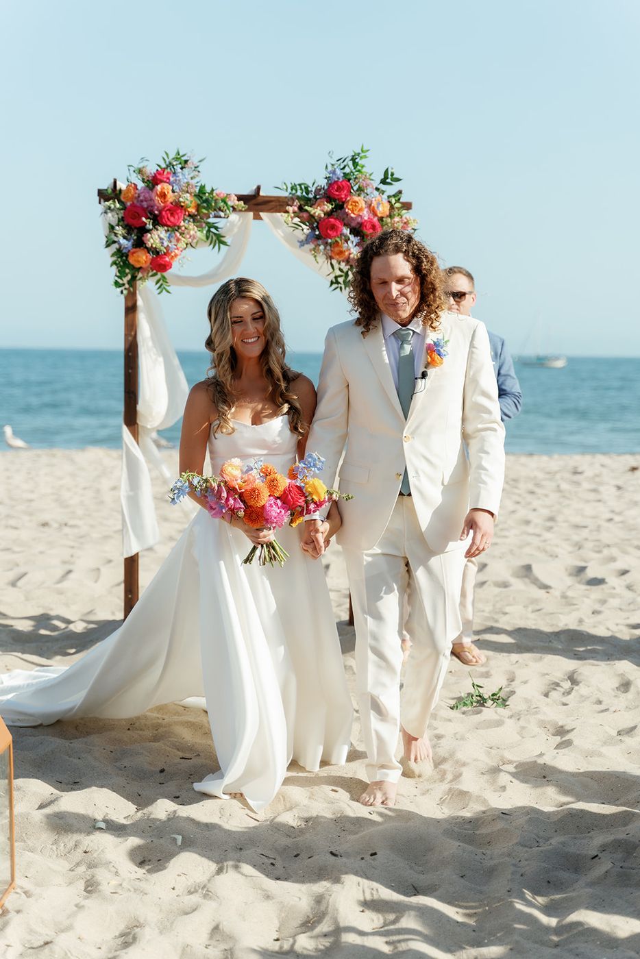 A wedding party on the sand beneath a floral arch