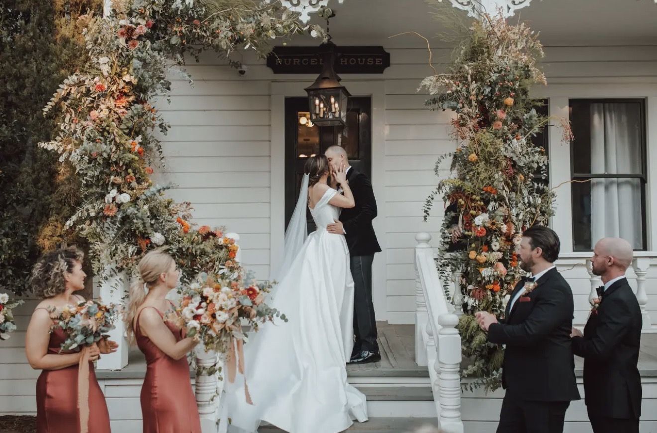 An outdoor ceremony under a floral arch on a white porch